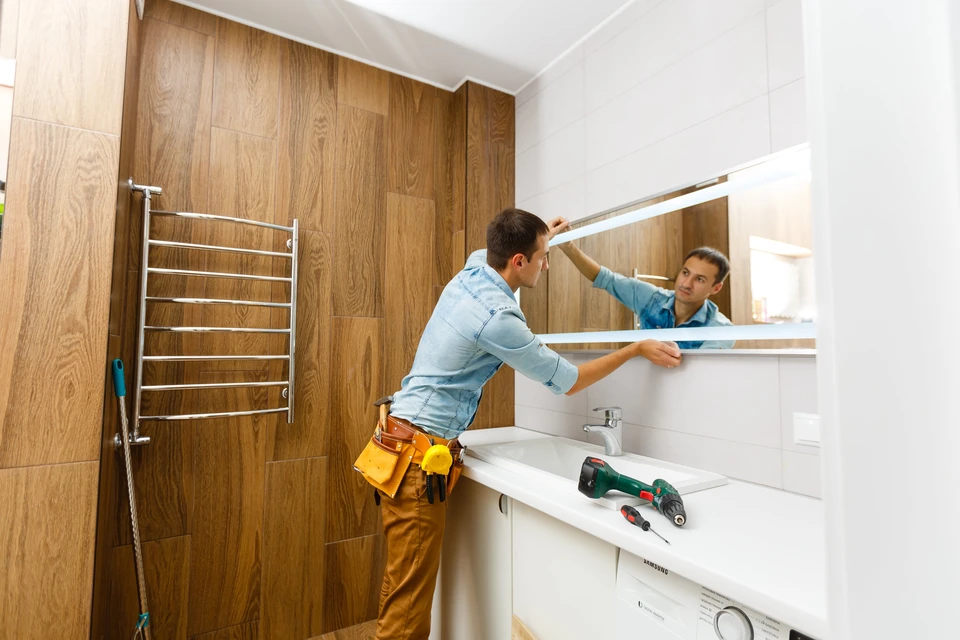 Un artisan installe un miroir dans une salle de bain moderne avec carrelage imitation bois