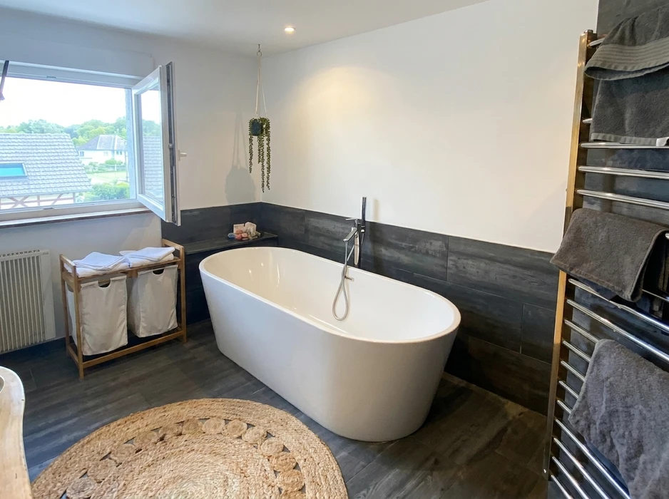 Salle de bain moderne avec baignoire îlot autoportante blanche, robinetterie colonne chromée sur carrelage imitation bois gris foncé