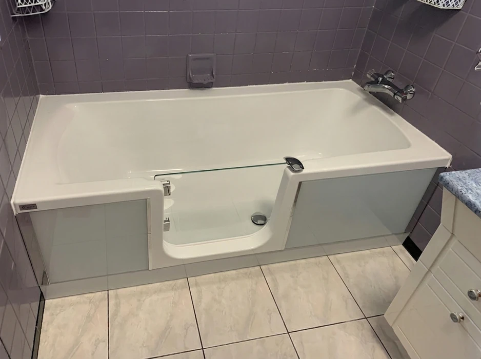 Salle de bain carrelée gris-mauve avec baignoire blanche à porte d'accès latérale intégrée, type baignoire à entrée facilitée pour personnes à mobilité réduite
