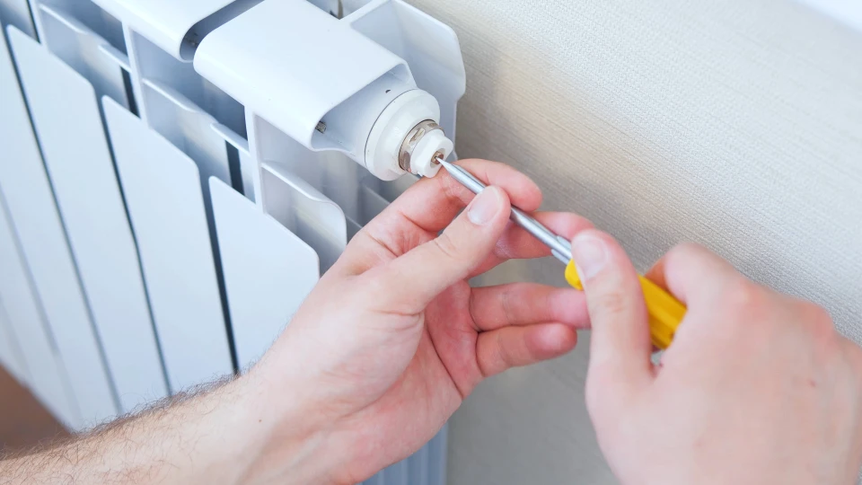 Homme effectuant maintenance sur radiateur domestique blanc, tenant tournevis jaune pour ajuster purgeur automatique