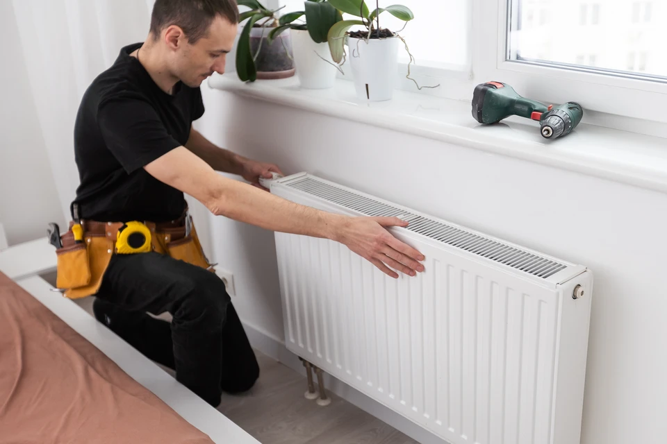 Technicien en salopette bleue effectuant la maintenance d'un radiateur à ailettes dans un intérieur résidentiel moderne