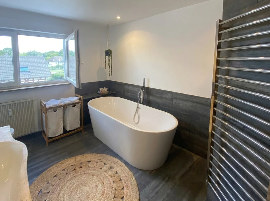 Deux plombiers en salopette bleue et casquette installent un lavabo vasque rond blanc sur plan de travail bois dans une salle de bain moderne