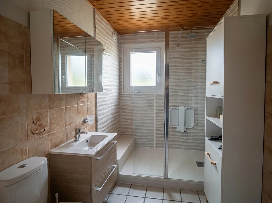 Salle de bain moderne sous combles avec meuble vasque suspendu en bois foncé, 3 tiroirs à poignées chromées, vasque céramique blanche encastrée, mitigeur monotrou chromé